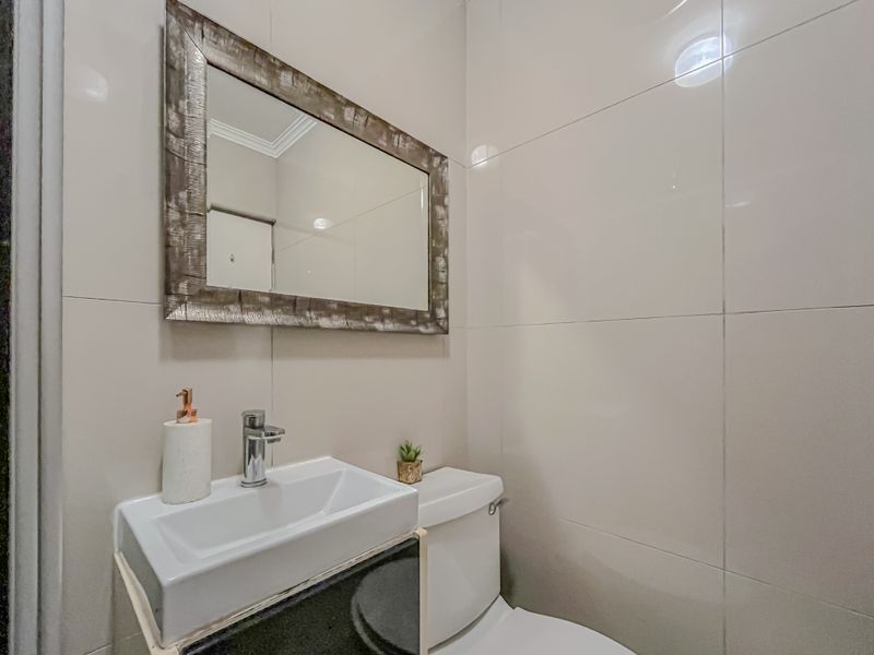 A compact, modern bathroom featuring a sleek ceramic basin with a chrome mixer tap, vanity cabinet, and a wall-mounted mirror against tiled walls.