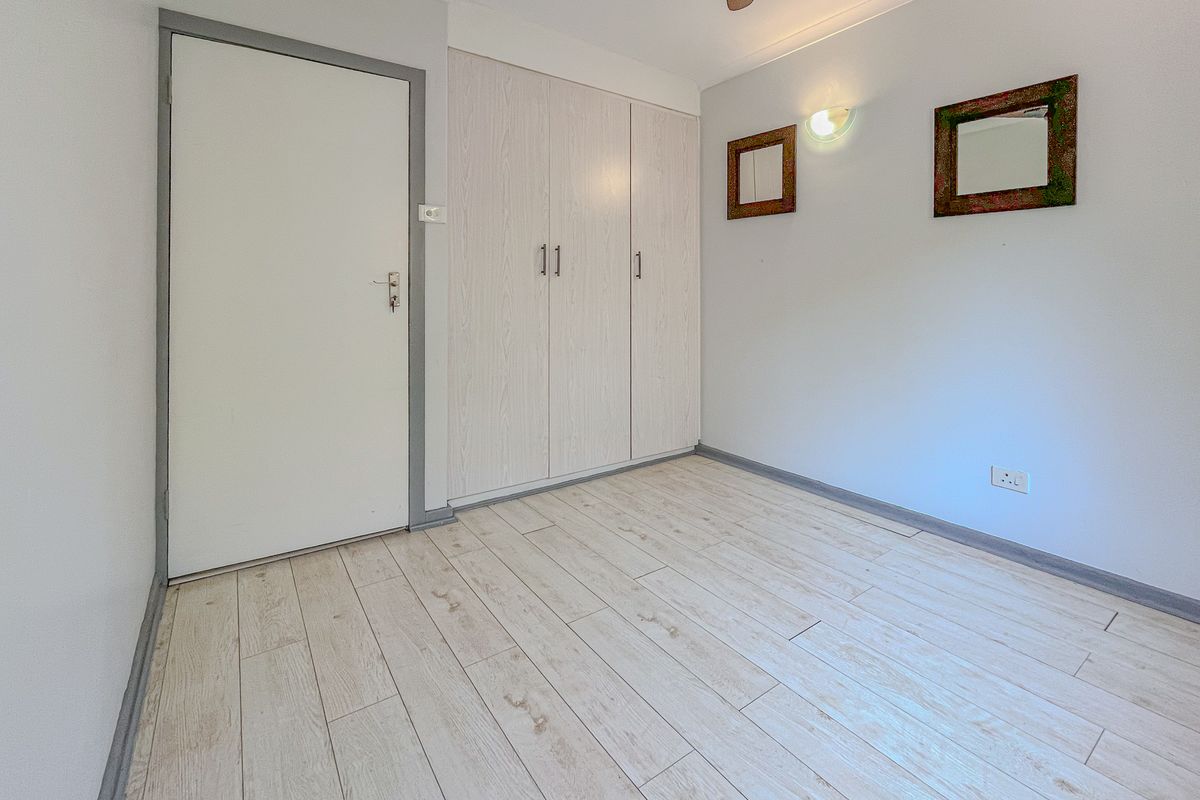 A bright, empty bedroom featuring light wood-look tile flooring, built-in cupboards, and a ceiling fan, offering a clean and neutral space.