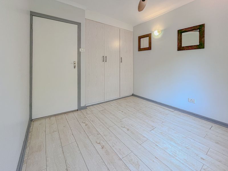 A bright, empty bedroom featuring light wood-look tile flooring, built-in cupboards, and a ceiling fan, offering a clean and neutral space.