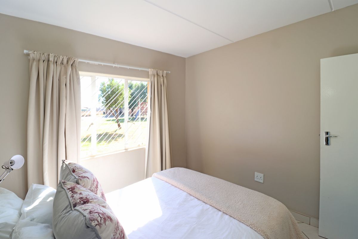 A well-maintained bedroom featuring neutral wall tones, a window with security bars, and a standard internal door.