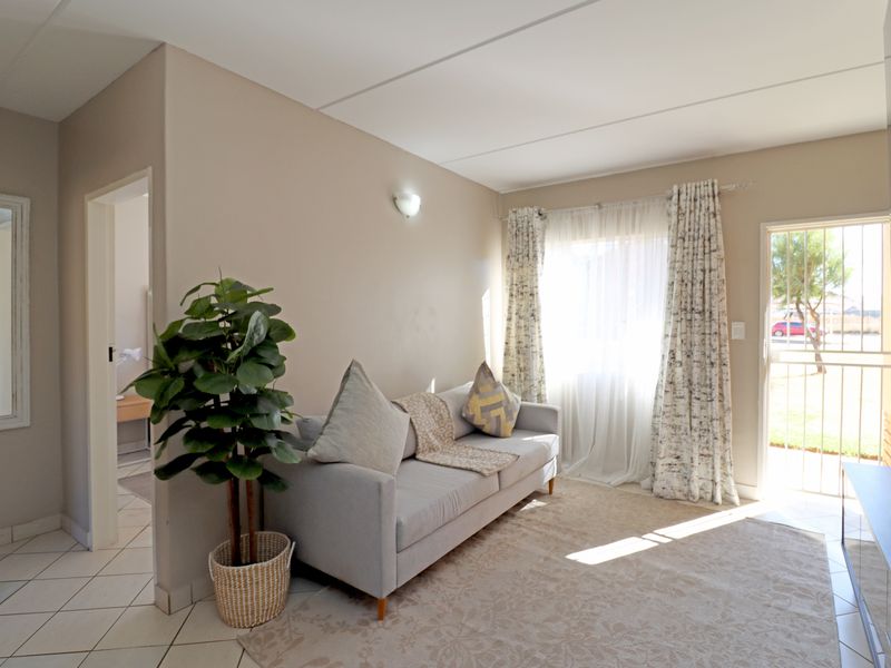 A bright living room featuring tiled flooring, a security gate entrance, and neutral wall finishes, offering a functional and well-lit living space.
