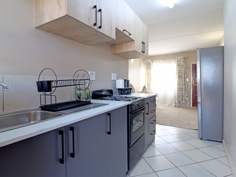 A functional kitchen featuring modern grey lower cabinetry, light wood-toned upper cabinets, tiled flooring, and a stainless steel sink with a freestanding stove.