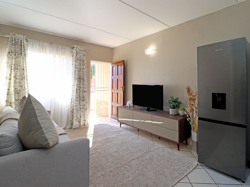 A functional living room featuring tiled flooring, wall sconce lighting, and direct access to an exterior entrance through a secure timber door.