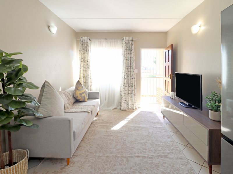 A bright and functional living room featuring tiled flooring, wall-mounted lighting, and direct access to an exterior security gate.