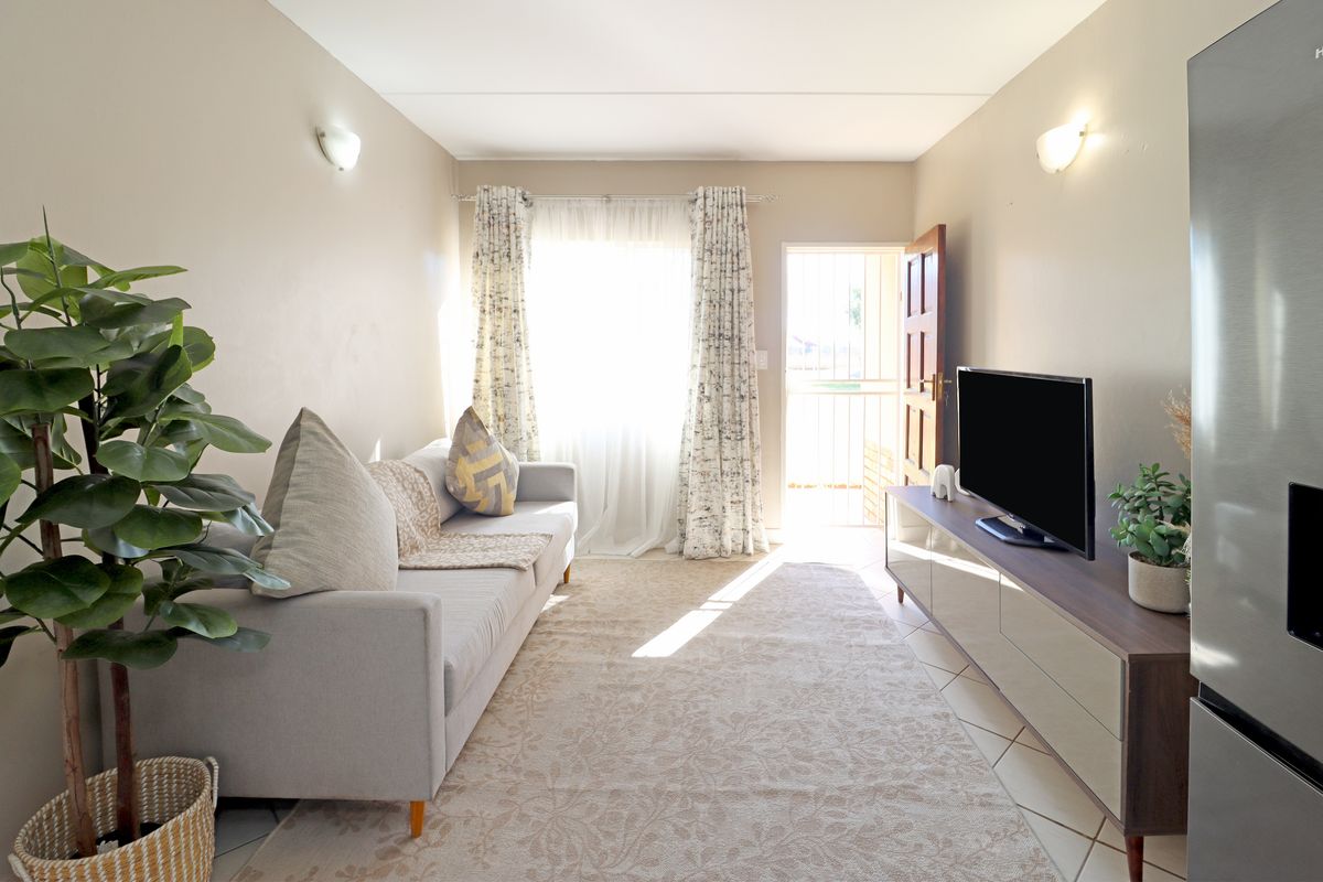 A bright and functional living room featuring tiled flooring, wall-mounted lighting, and direct access to an exterior security gate.