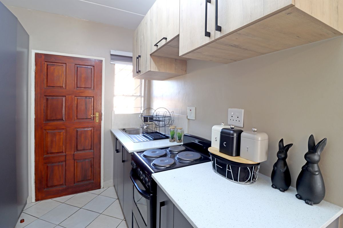 A functional kitchen featuring modern light wood cabinetry, dark base units, a stainless steel sink, and an electric stove with tiled flooring.