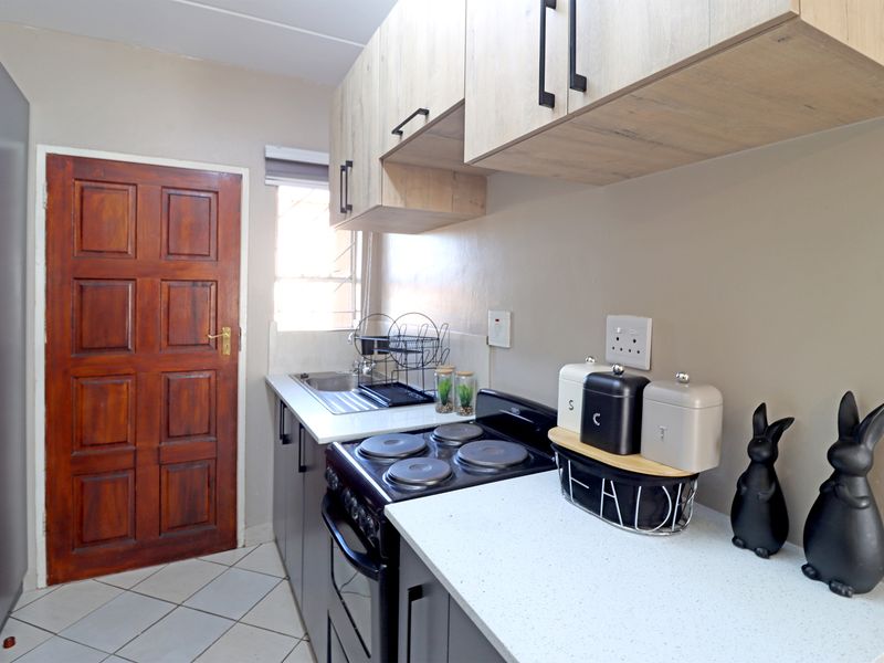 A functional kitchen featuring modern light wood cabinetry, dark base units, a stainless steel sink, and an electric stove with tiled flooring.