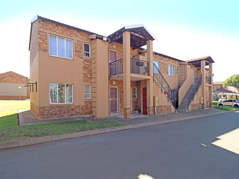 A two-story apartment building featuring a face brick facade, external staircases, and private balconies, situated in a well-maintained residential complex.