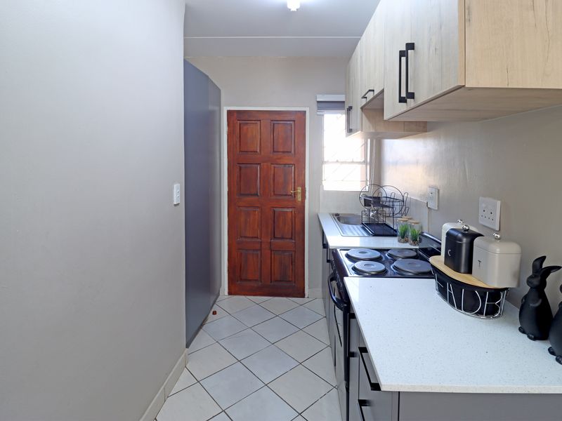 A functional kitchen featuring modern light wood cabinetry, stone countertops, an integrated electric hob and oven, and durable tiled flooring.