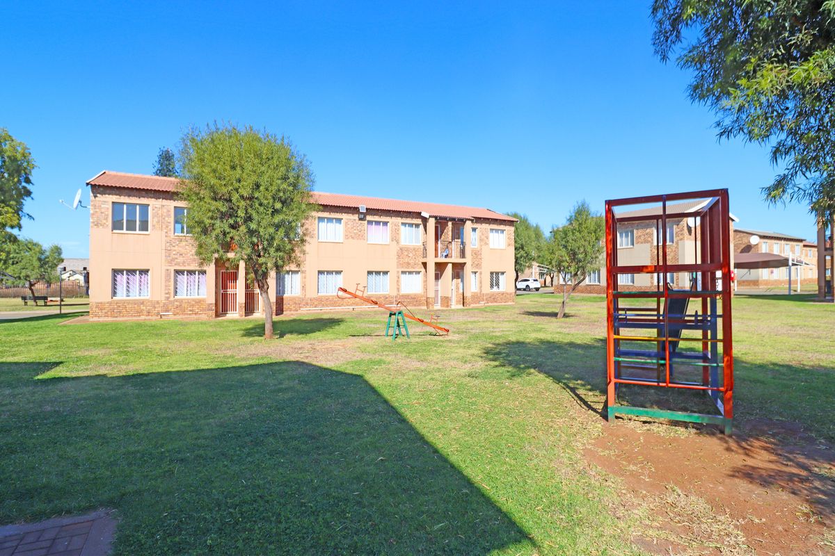 Exterior view of a multi-story apartment complex featuring a communal garden area with playground equipment and brick facade construction.