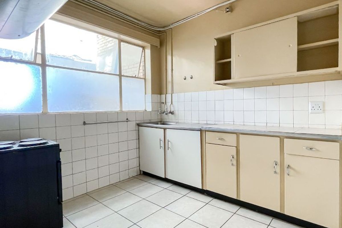 A functional, dated kitchen featuring tiled flooring, a tiled splashback, built-in cabinetry, and a stainless steel sink, ready for modernization.