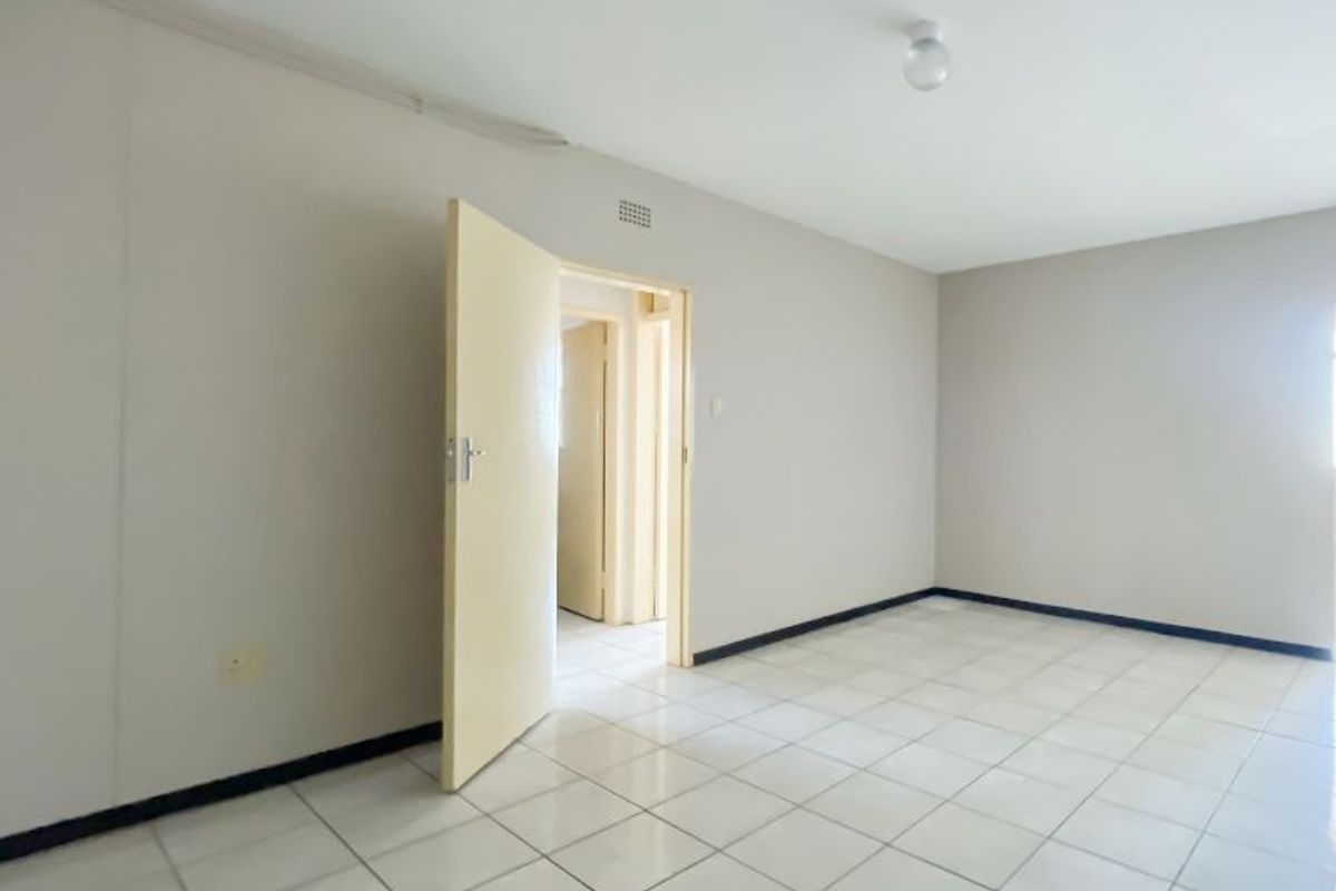 An empty bedroom featuring tiled flooring, neutral walls, and a doorway leading to an adjacent hallway.