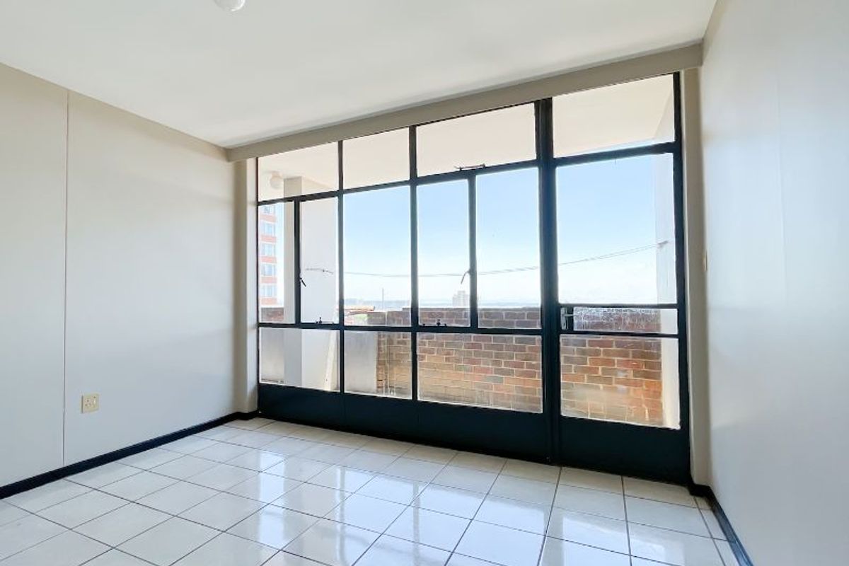 An empty living room featuring large steel-framed windows that provide ample natural light and access to an outdoor balcony area.