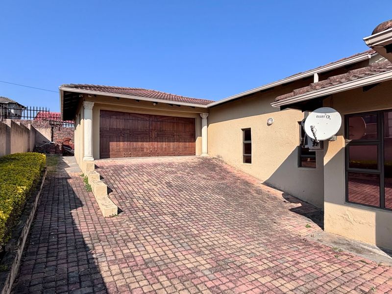 Front exterior view featuring a paved driveway leading to a double garage with wooden doors and a tiled roof.