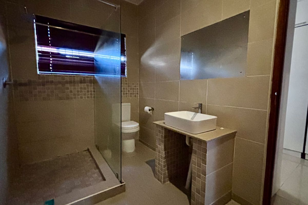 Modern bathroom featuring a glass-enclosed shower, vessel sink on a tiled vanity, and neutral wall tiling throughout.