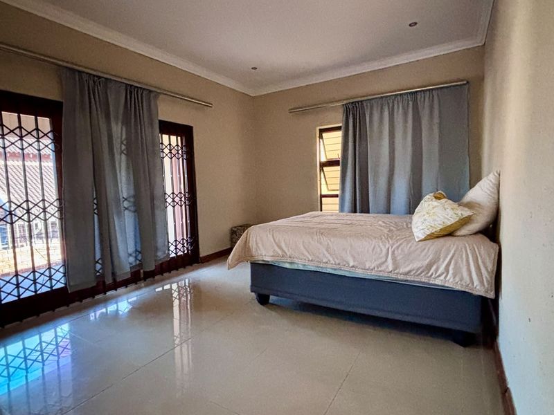Spacious bedroom featuring tiled flooring, recessed lighting, and sliding doors with security gates leading to an outdoor area.