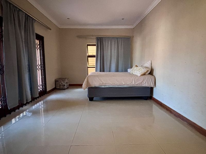 Spacious bedroom featuring tiled flooring, a sliding door with security gate, and neutral wall finishes.