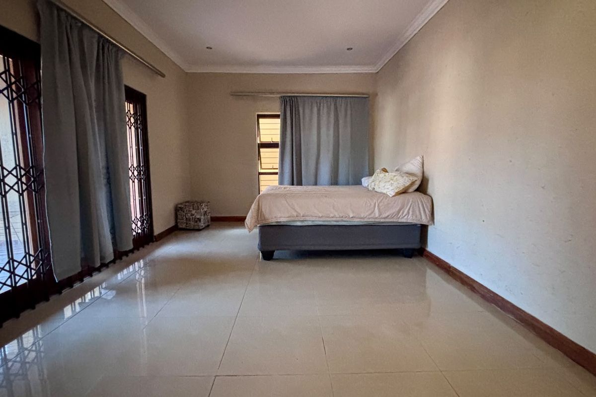 Spacious bedroom featuring tiled flooring, a sliding door with security gate, and neutral wall finishes.
