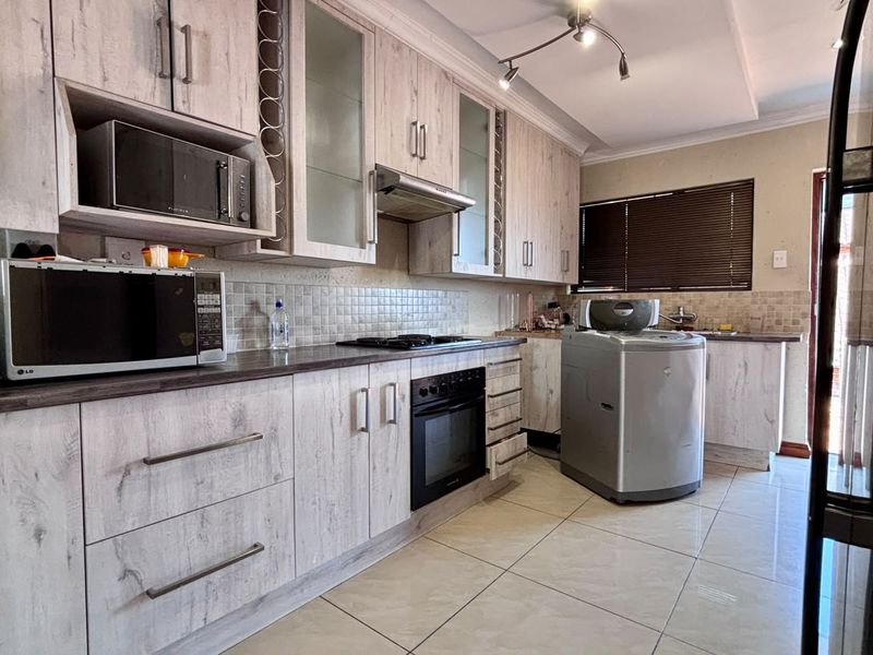 A functional kitchen featuring light wood-grain cabinetry, tiled backsplash, built-in oven with gas hob, and tiled flooring throughout.