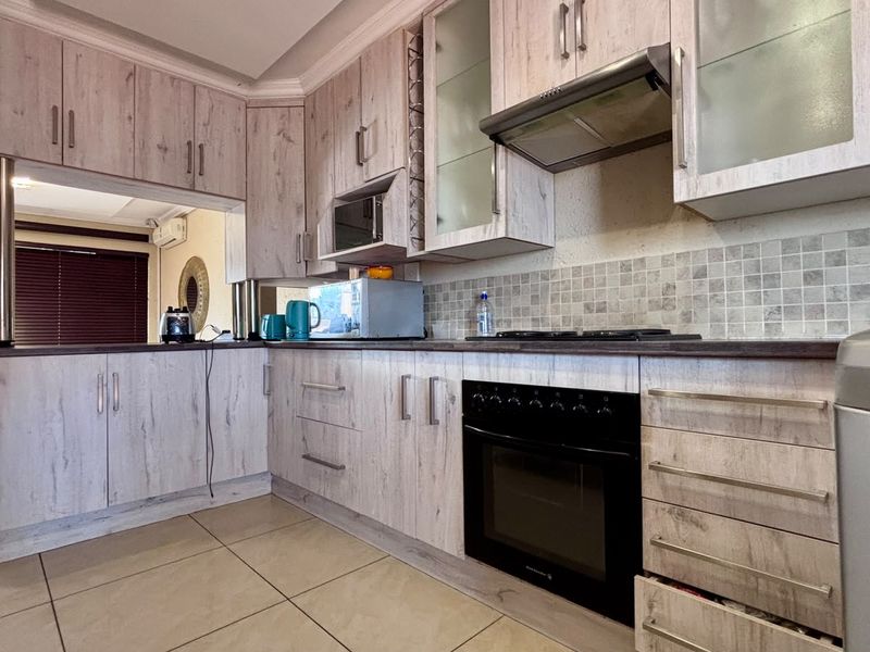 A functional kitchen featuring light wood-grain cabinetry, tiled backsplash, built-in oven, gas hob, and extractor fan, with tiled flooring throughout.