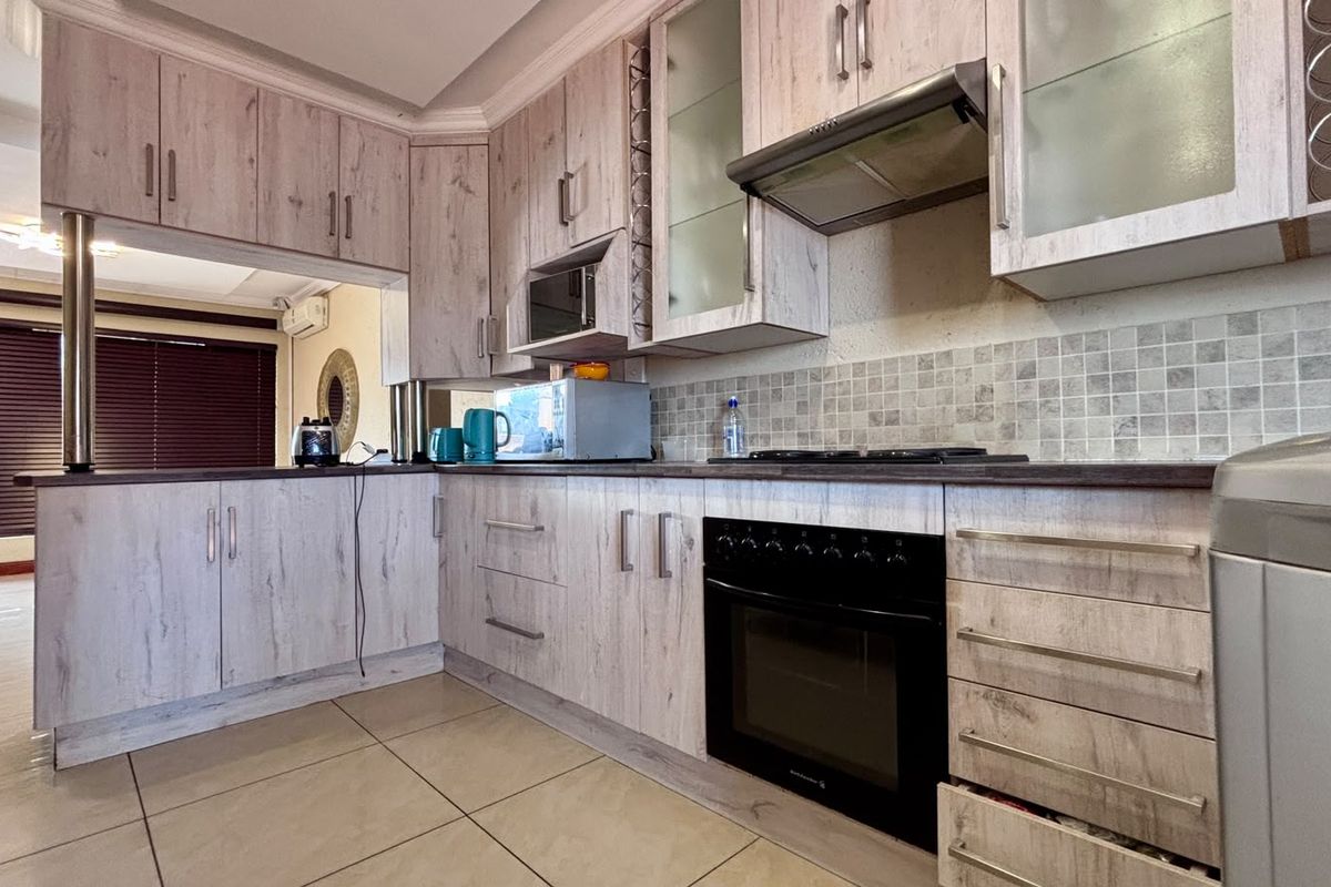 A functional kitchen featuring light wood-grain cabinetry, tiled backsplash, built-in oven, gas hob, and extractor fan, with tiled flooring throughout.