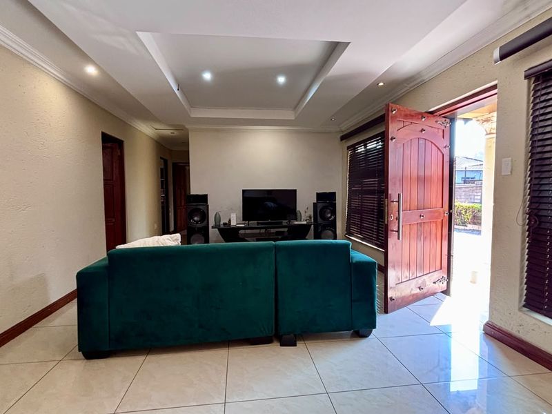 A spacious living room featuring tiled flooring, a recessed ceiling with downlights, and direct access to the exterior through a wooden door.