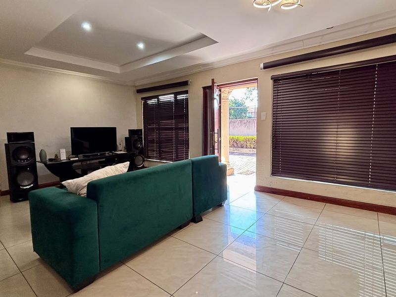 Spacious living room featuring large format floor tiles, recessed ceiling detail, and natural light through venetian blinds with direct access to the outdoor area.
