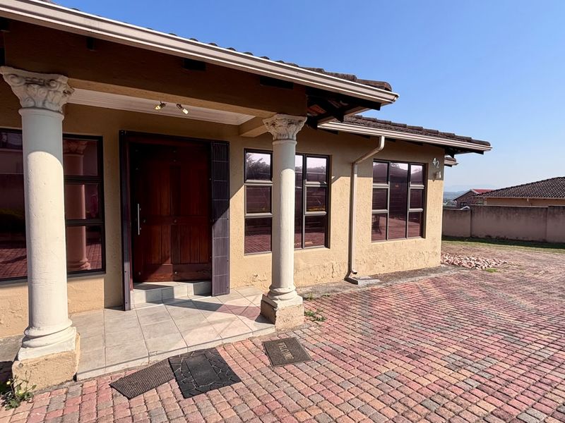Front entrance of the house featuring a covered porch with decorative columns, timber door, and a paved driveway area.