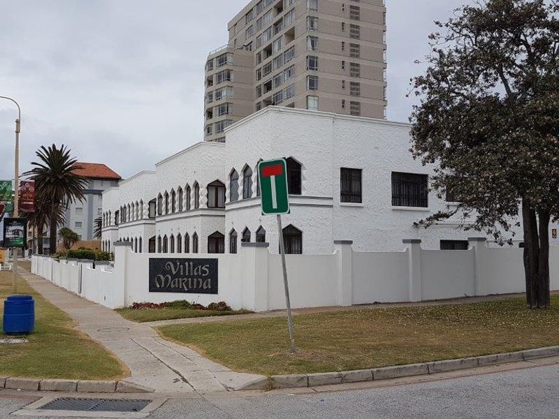 Street view of the Villas Marina apartment complex, featuring a white facade with arched windows and a secure boundary wall.