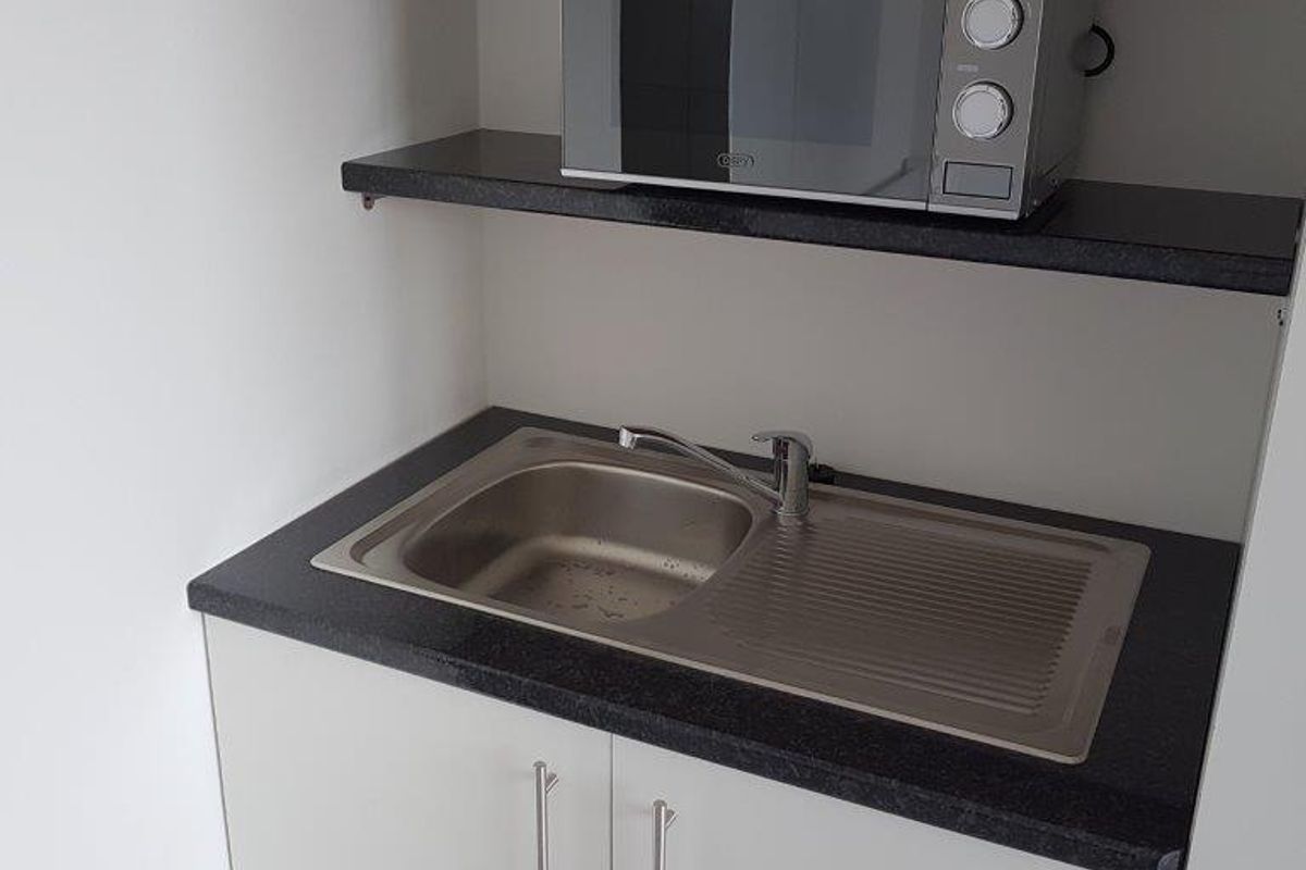 A compact scullery or utility area featuring a stainless steel sink, dark laminate countertop, and clean white cabinetry with overhead shelving.