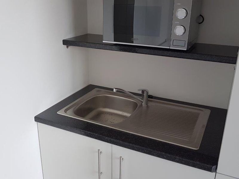A compact scullery or utility area featuring a stainless steel sink, dark laminate countertop, and clean white cabinetry with overhead shelving.