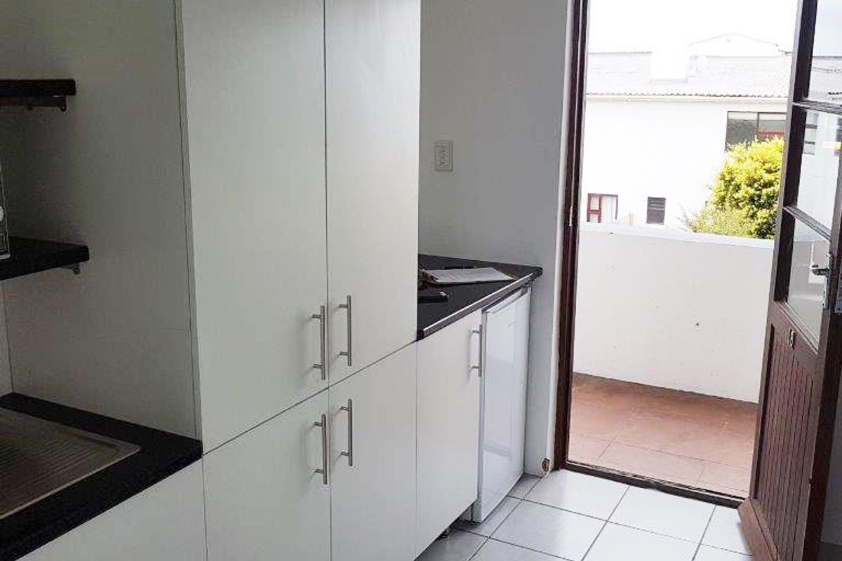A clean, functional scullery or utility area featuring white built-in cabinetry, dark countertops, and direct access to an outdoor balcony area.