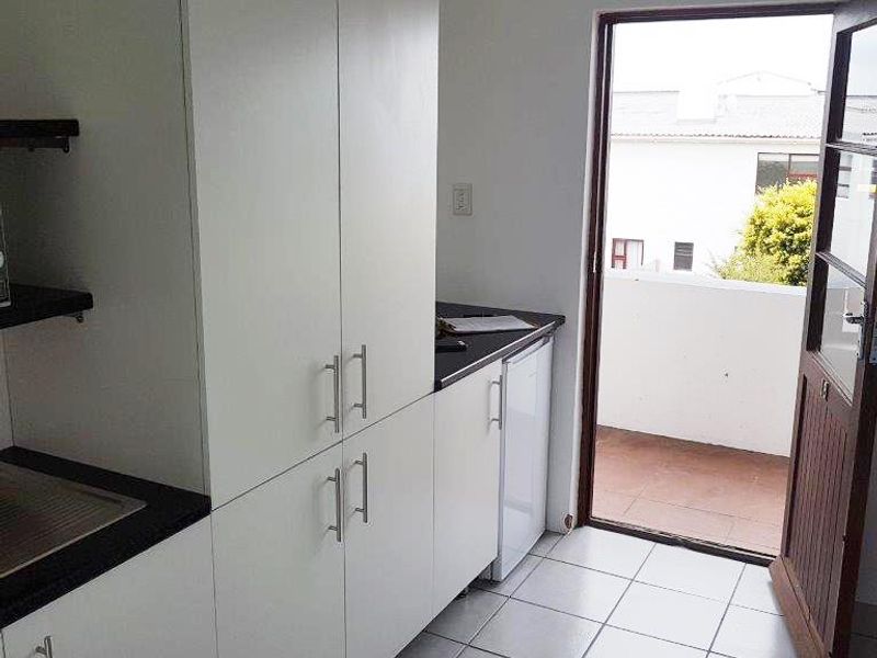 A clean, functional scullery or utility area featuring white built-in cabinetry, dark countertops, and direct access to an outdoor balcony area.