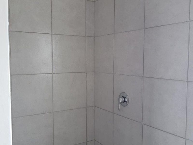 A clean, modern shower enclosure featuring neutral grey wall tiles and chrome shower fixtures.