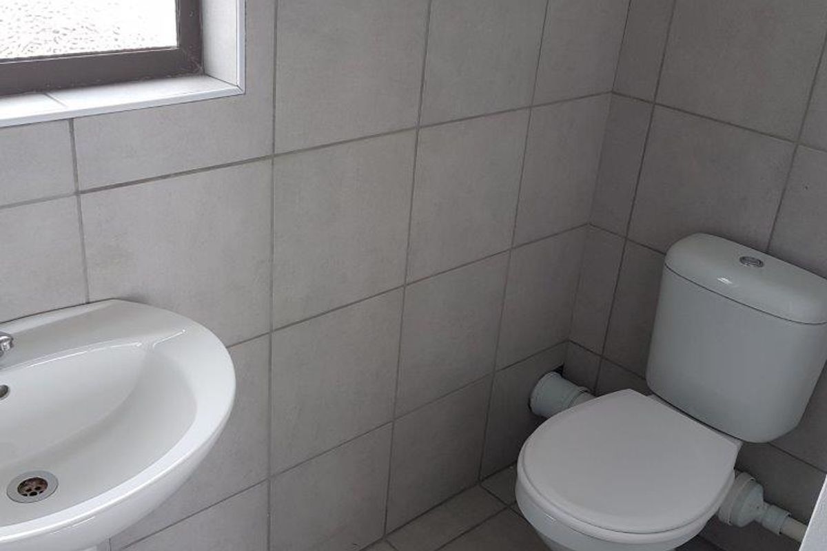 A clean, functional bathroom featuring a pedestal basin, a standard toilet, and neutral grey ceramic wall and floor tiling.