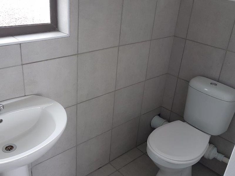 A clean, functional bathroom featuring a pedestal basin, a standard toilet, and neutral grey ceramic wall and floor tiling.