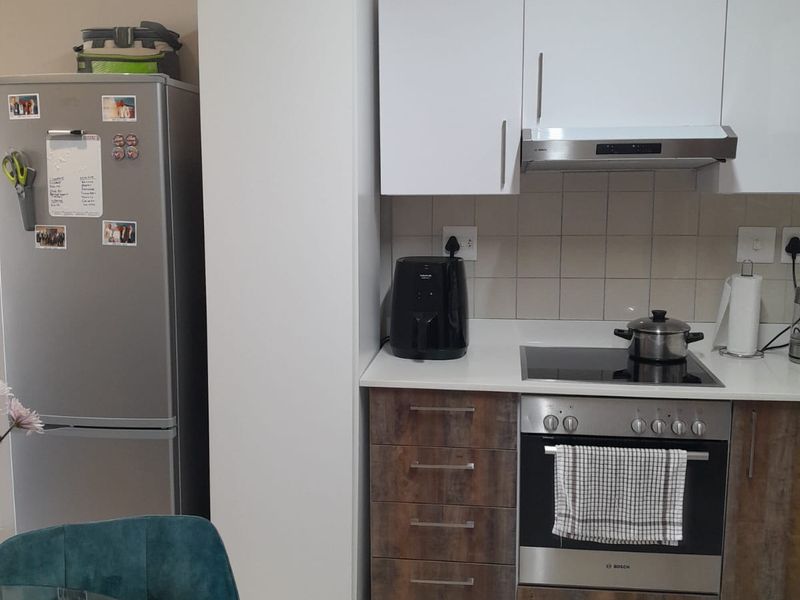 A modern kitchen featuring white upper cabinets, wood-finish lower cabinetry, stone countertops, and integrated stainless steel appliances including an oven and extractor fan.