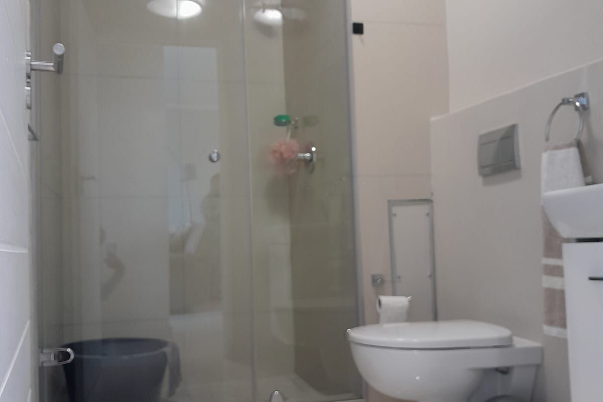 A modern bathroom featuring a glass-enclosed shower, wall-mounted toilet, and neutral tiled finishes throughout.