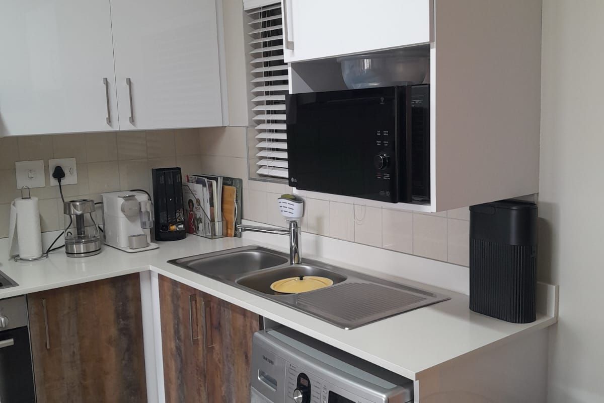 Compact kitchen featuring modern white and wood-grain cabinetry, stainless steel sink, integrated washing machine, and built-in oven with tiled backsplash.
