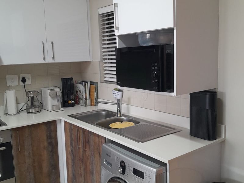 Compact kitchen featuring modern white and wood-grain cabinetry, stainless steel sink, integrated washing machine, and built-in oven with tiled backsplash.