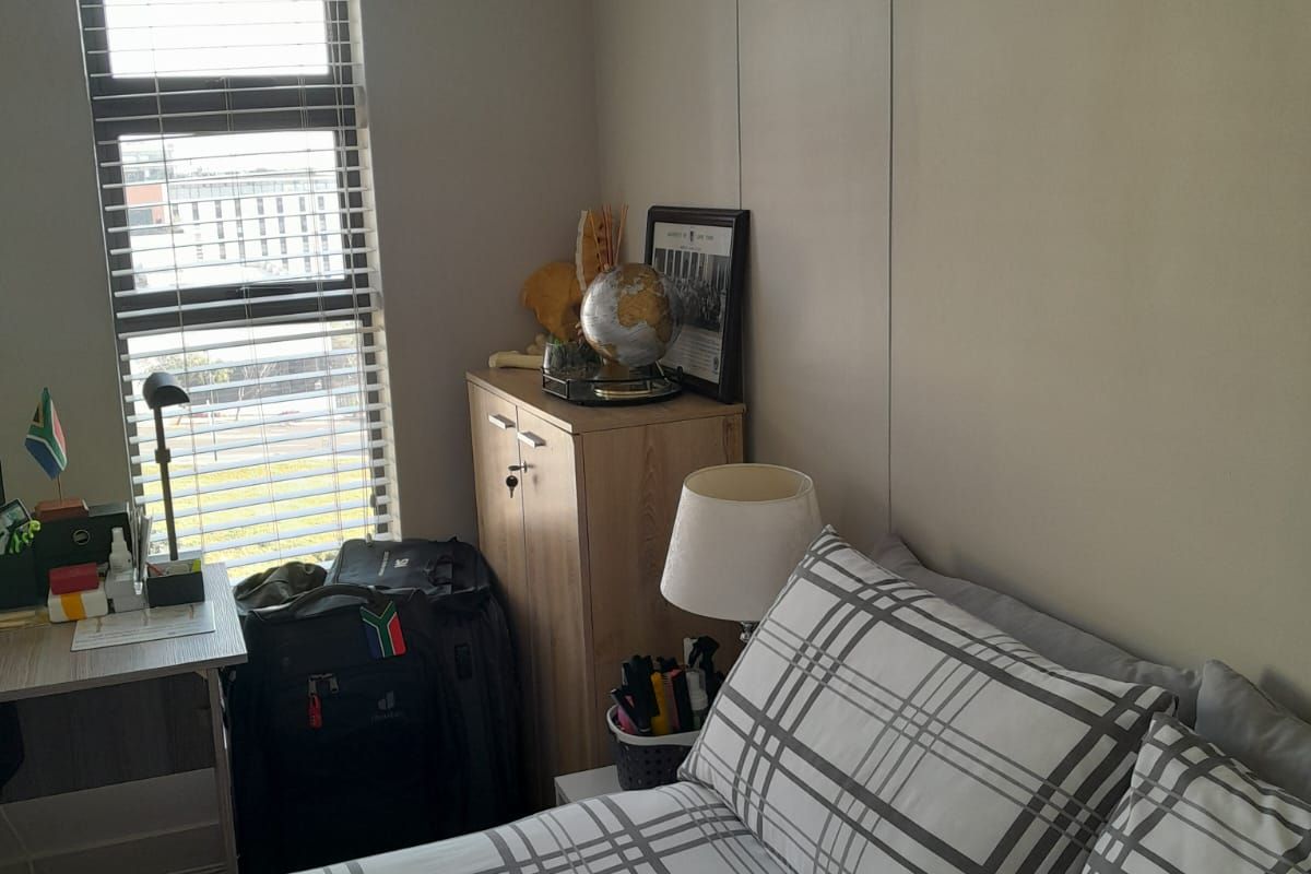A functional bedroom featuring a window with venetian blinds, providing natural light and a view of the surrounding area.