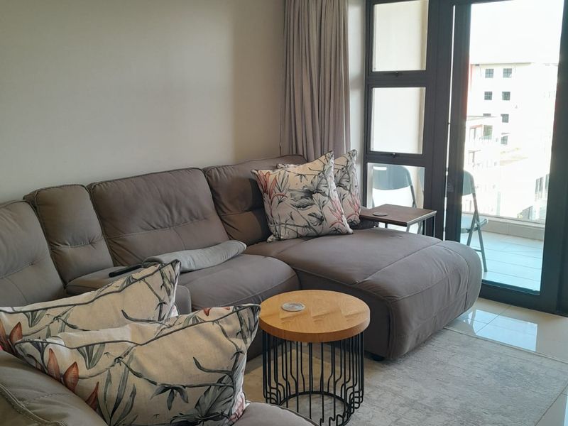 A well-maintained living room featuring tiled floors, recessed lighting, and a large sliding glass door providing access to an outdoor balcony area.