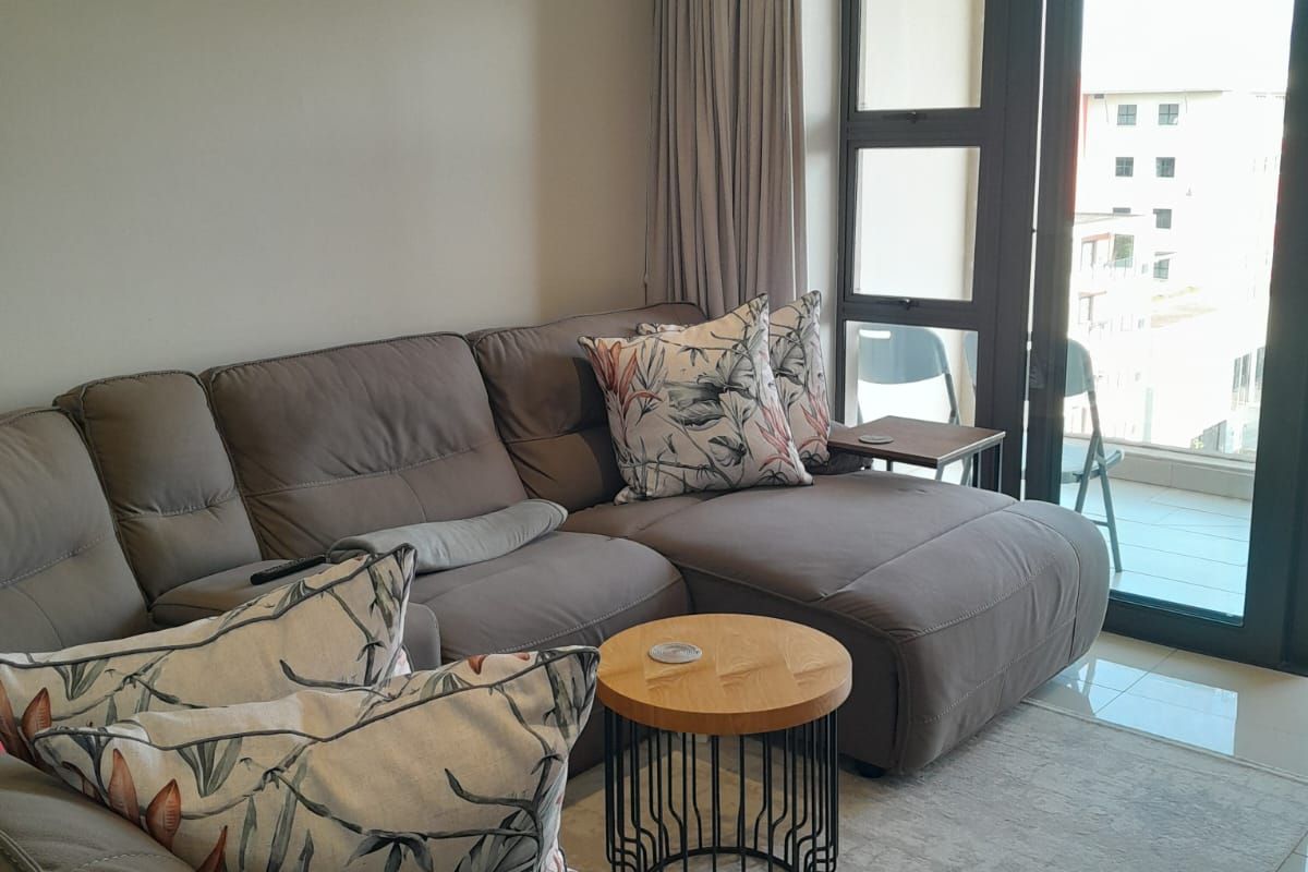 A well-maintained living room featuring tiled floors, recessed lighting, and a large sliding glass door providing access to an outdoor balcony area.