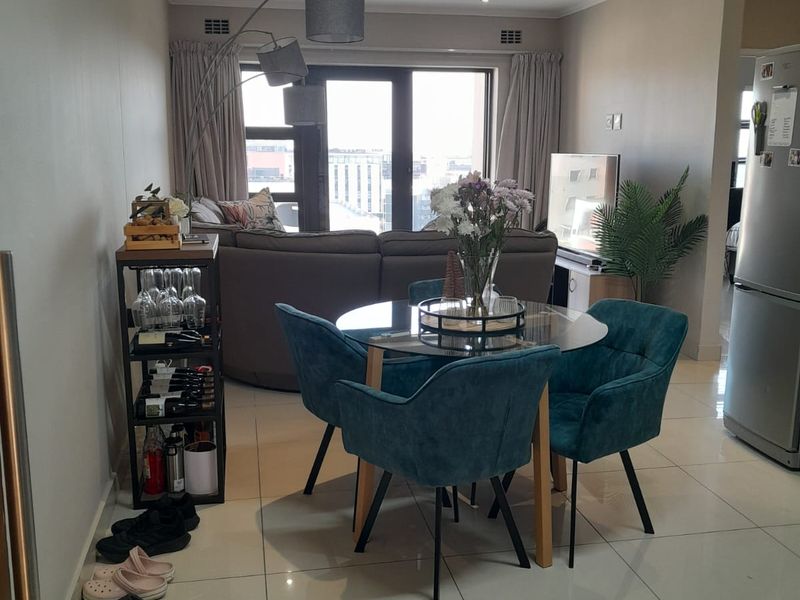 Open-plan living and dining area featuring polished porcelain floor tiles, recessed downlighting, and large sliding glass doors leading to a balcony.