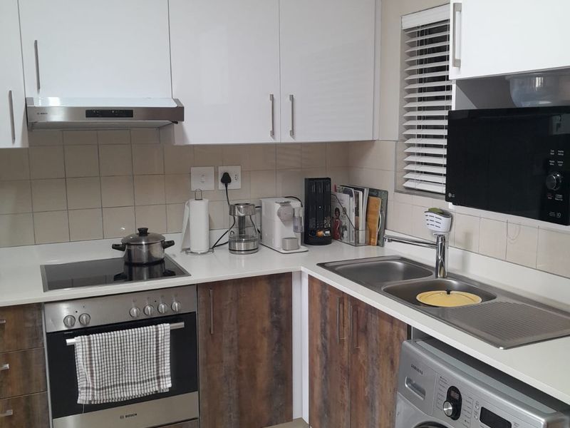 A functional kitchen featuring modern white and wood-grain cabinetry, integrated appliances including an oven and hob, and a stainless steel sink.