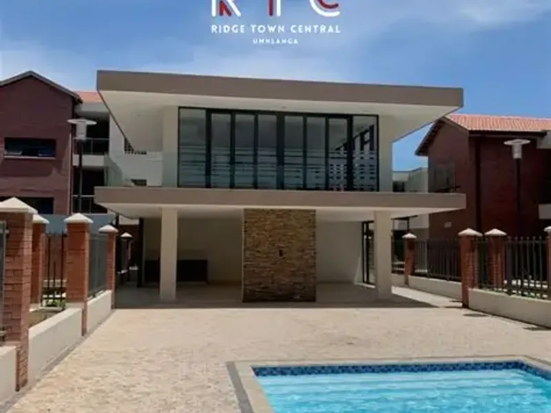 A well-maintained communal pool area featuring a paved courtyard, stone-clad feature wall, and a covered patio space within a modern apartment complex.