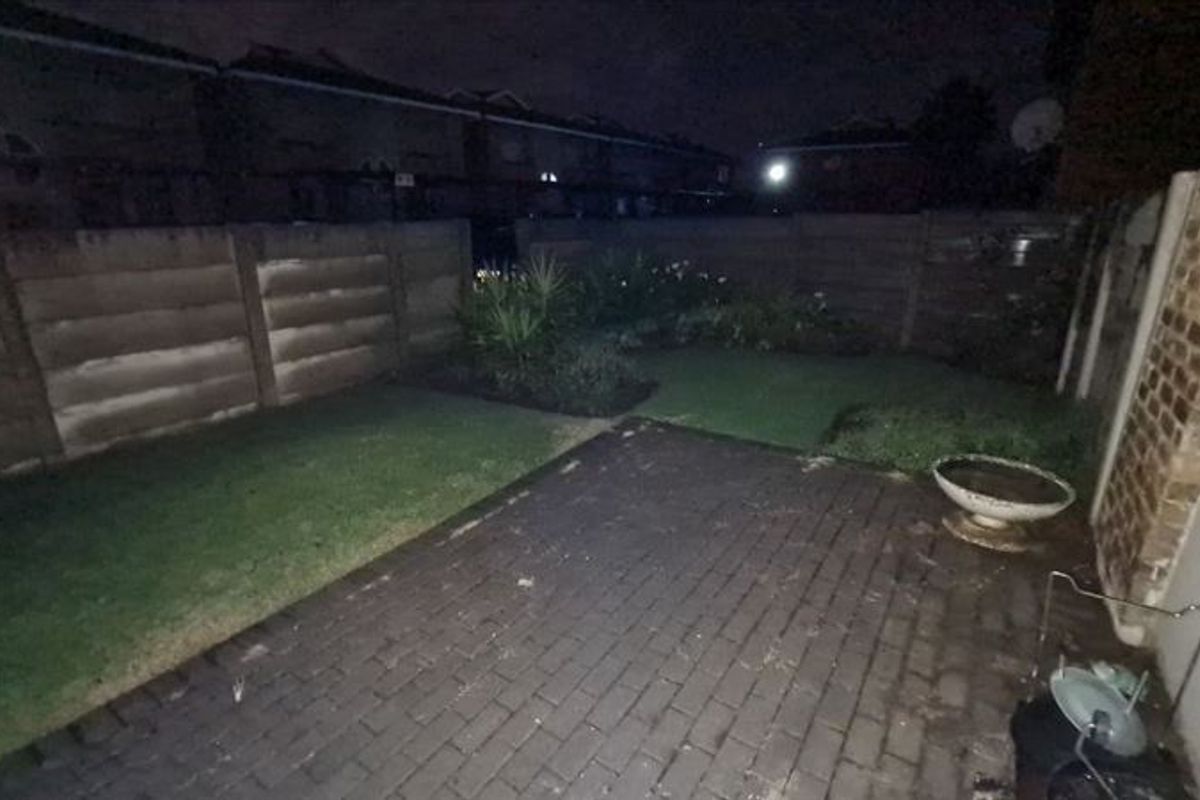 A rear garden area featuring a paved patio and a lawn enclosed by precast concrete boundary walls, captured at night.