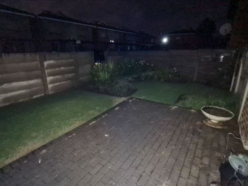A rear garden area featuring a paved patio and a lawn enclosed by precast concrete boundary walls, captured at night.