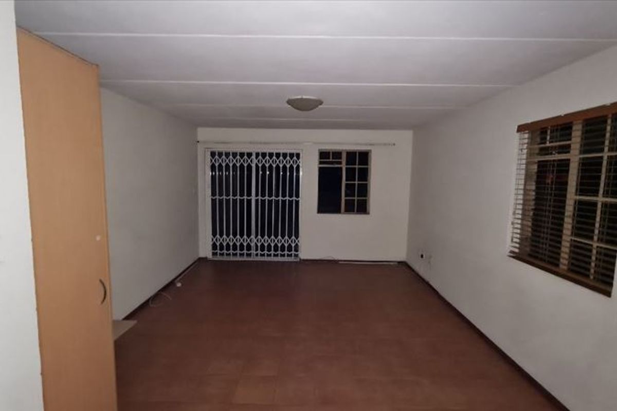 An empty, open-plan living area featuring tiled flooring, a built-in cupboard, and a security gate leading to the exterior.