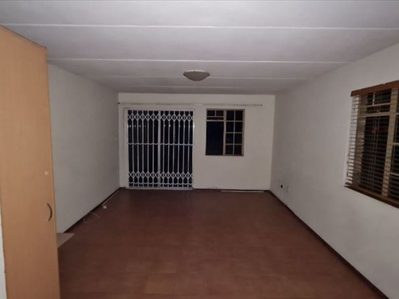 An empty, open-plan living area featuring tiled flooring, a built-in cupboard, and a security gate leading to the exterior.